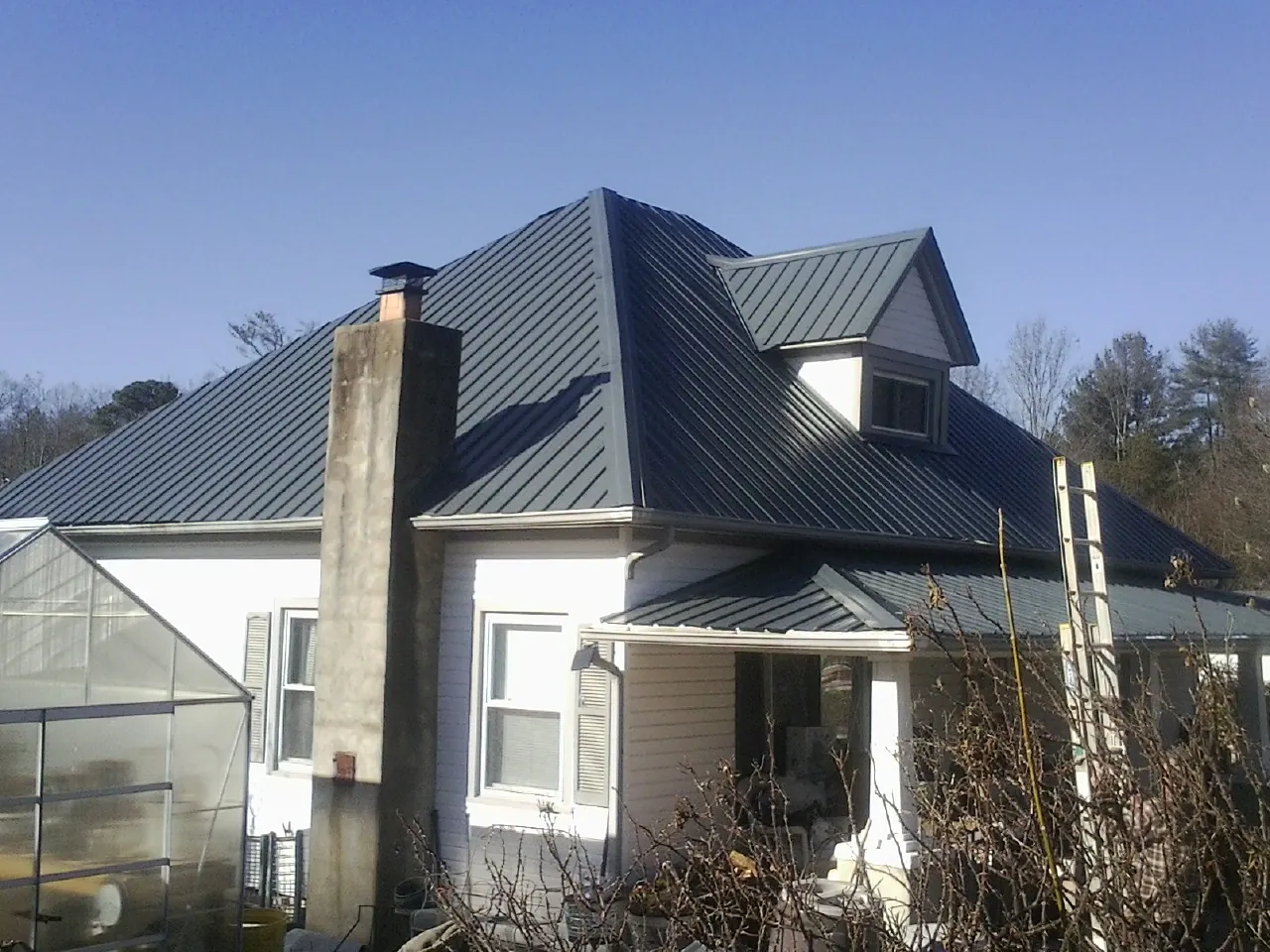 Dark blue standing seam metal roof on a white farmhouse with dormer — Slate & Tile Roof Repair by Roofing Brothers in Bottineau