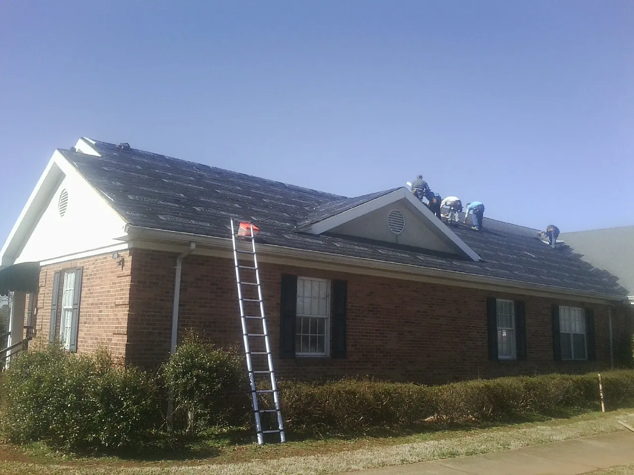 Crew tearing shingles off a brick ranch roof with a ladder set — Metal Roof Repair work by our crew in Bottineau