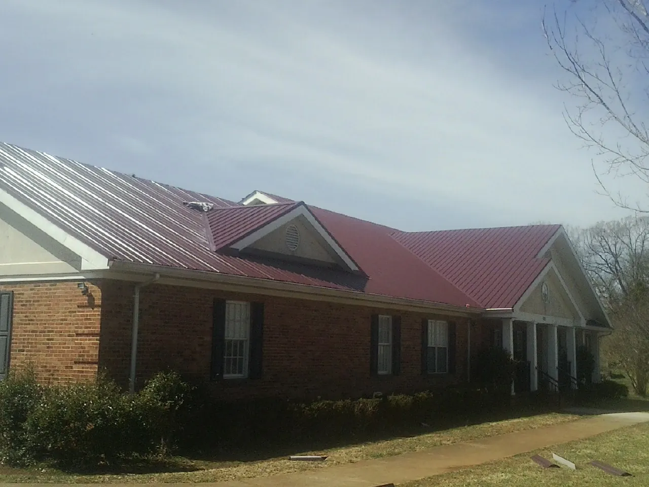 Red metal roof with gabled entries on a long brick building, from a Hail Damage Roof Repair job in Bottineau