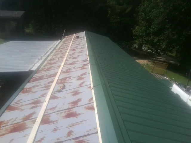Old rusted panels beside newly installed green metal roofing — Wind Damage Roof Repair by Roofing Brothers in Bottineau