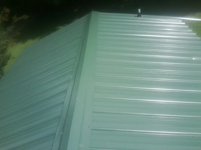New green metal panels meeting at the ridge of a roof — Flat Roof Repair work by our crew in Bottineau