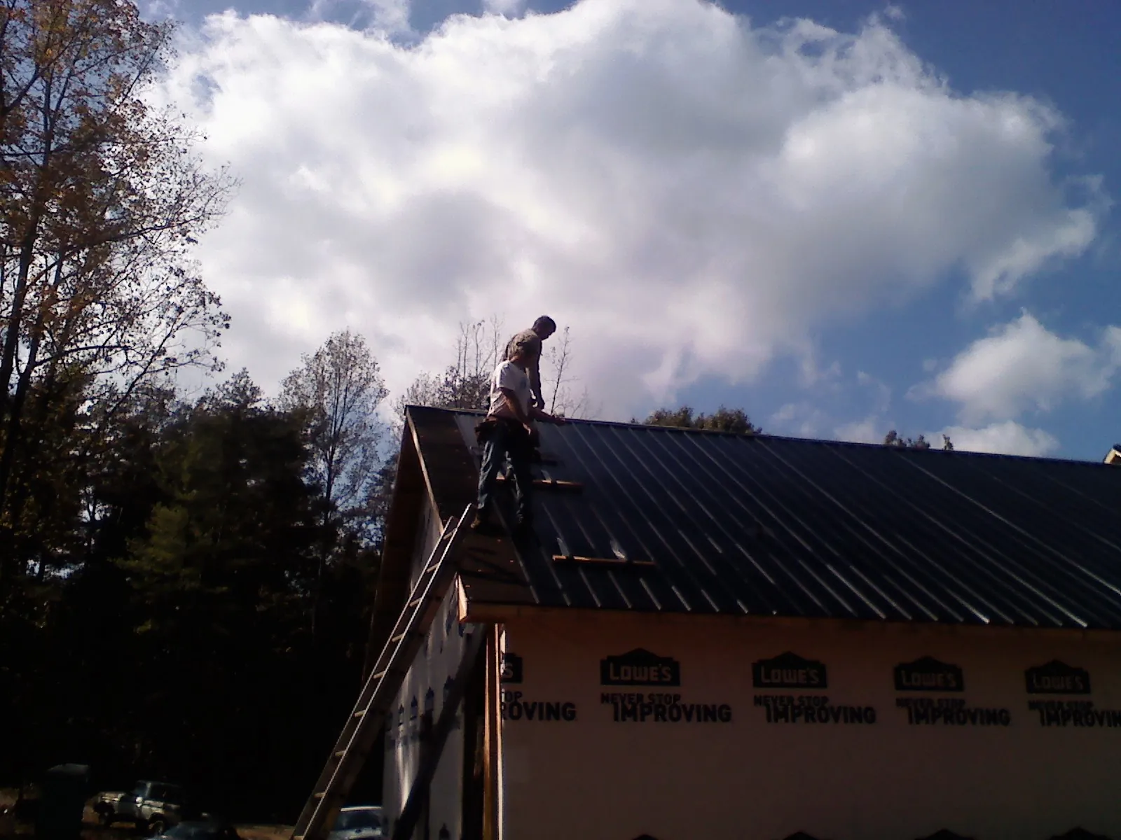 Roofer fastening dark metal panels high against a cloudy sky, from a Roof Inspection job in Bottineau