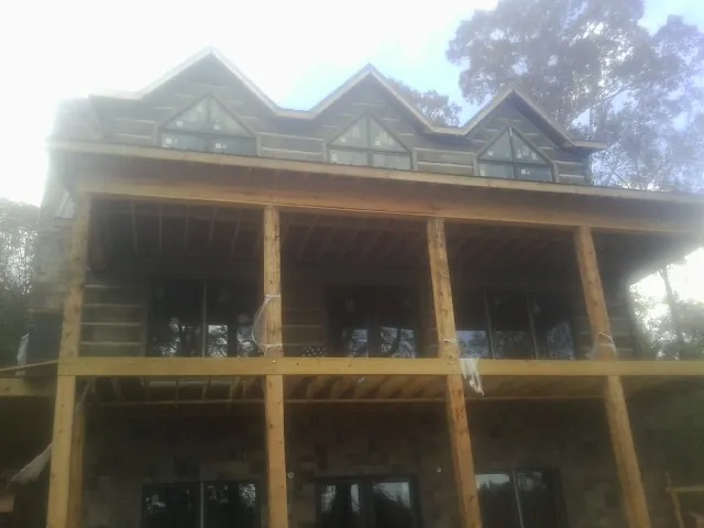 Dormers and porch framing on a large log home under construction — Roof Coating work by our crew in Bottineau