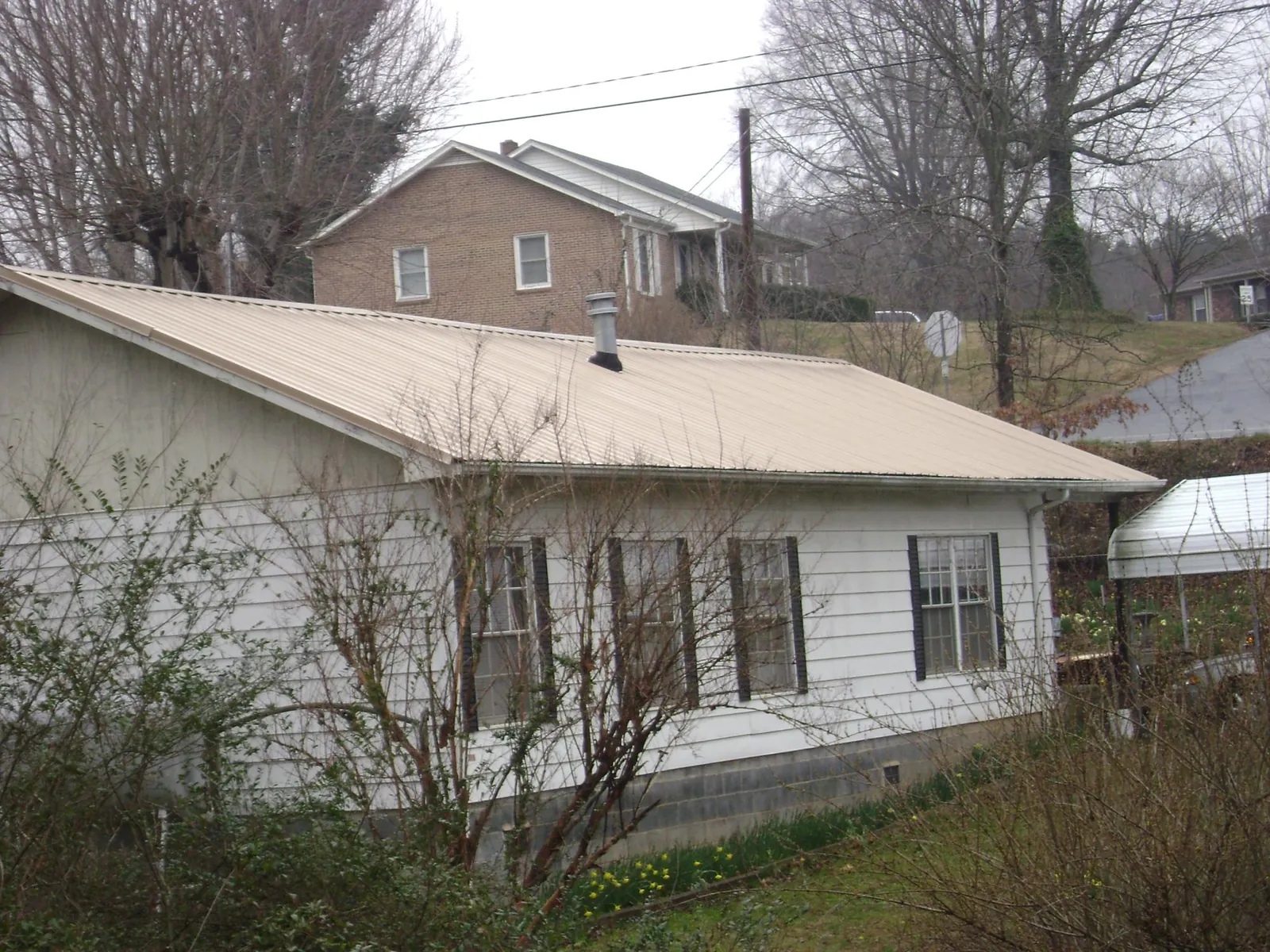 Tan metal roof on a white sided house set into a hillside — Commercial Roofing by Roofing Brothers in Bottineau