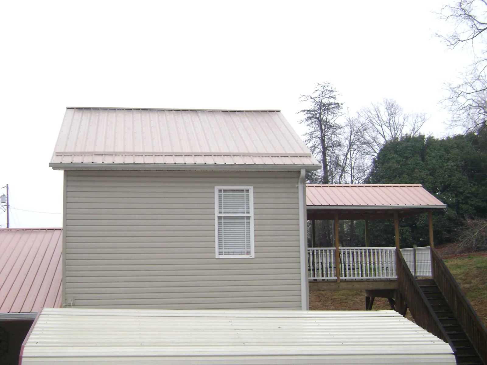 Tan metal roofs on a two story addition and attached porch, from a Roof Replacement job in Bottineau